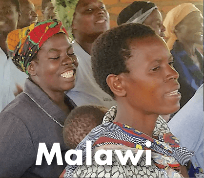 A smiling woman and child in a public gathering, representing Kupenda’s work in Malawi.