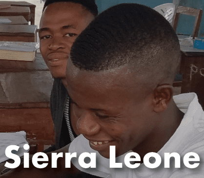 A young man with a buzz cut and a bright smile sits among others in a supportive learning environment.