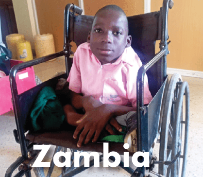 A boy sitting in a wheelchair wearing a pink and white shirt, looking directly at the camera.