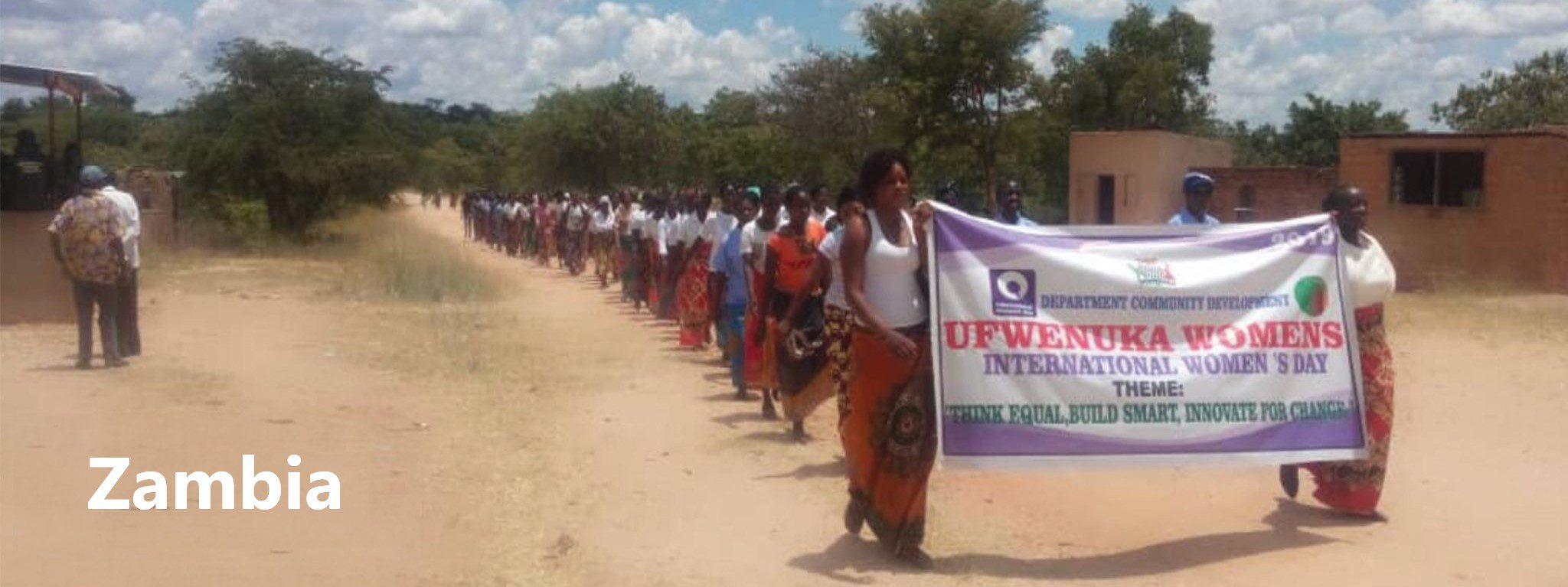 A group of people marching on a dirt road holding banners, advocating for disability justice and inclusion.