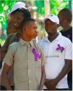 A group of boys and young men stand outdoors wearing purple ribbons on their shirts in recognition of International Epilepsy Day, with trees and greenery in the background.