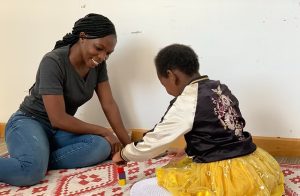 A woman seated on the floor, playing with a young girl.