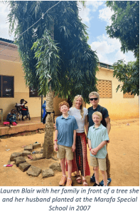 The author and her family pose beneath a tree outside a school in Kenya, with students in the background