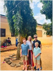 The author and her family pose beneath a tree outside a school in Kenya, with students in the background