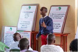George shares his testimony during a disability advocacy workshop for Christian leaders in Kenya, with disability and faith discussion materials displayed behind him