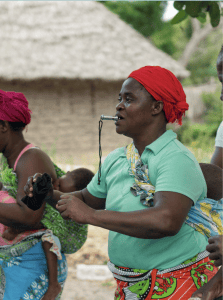 Nikiti blowing a whistle and dancing surrounded by other women carrying children